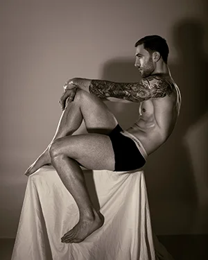 Ritts inspired male tattooed model sitting stool sepia